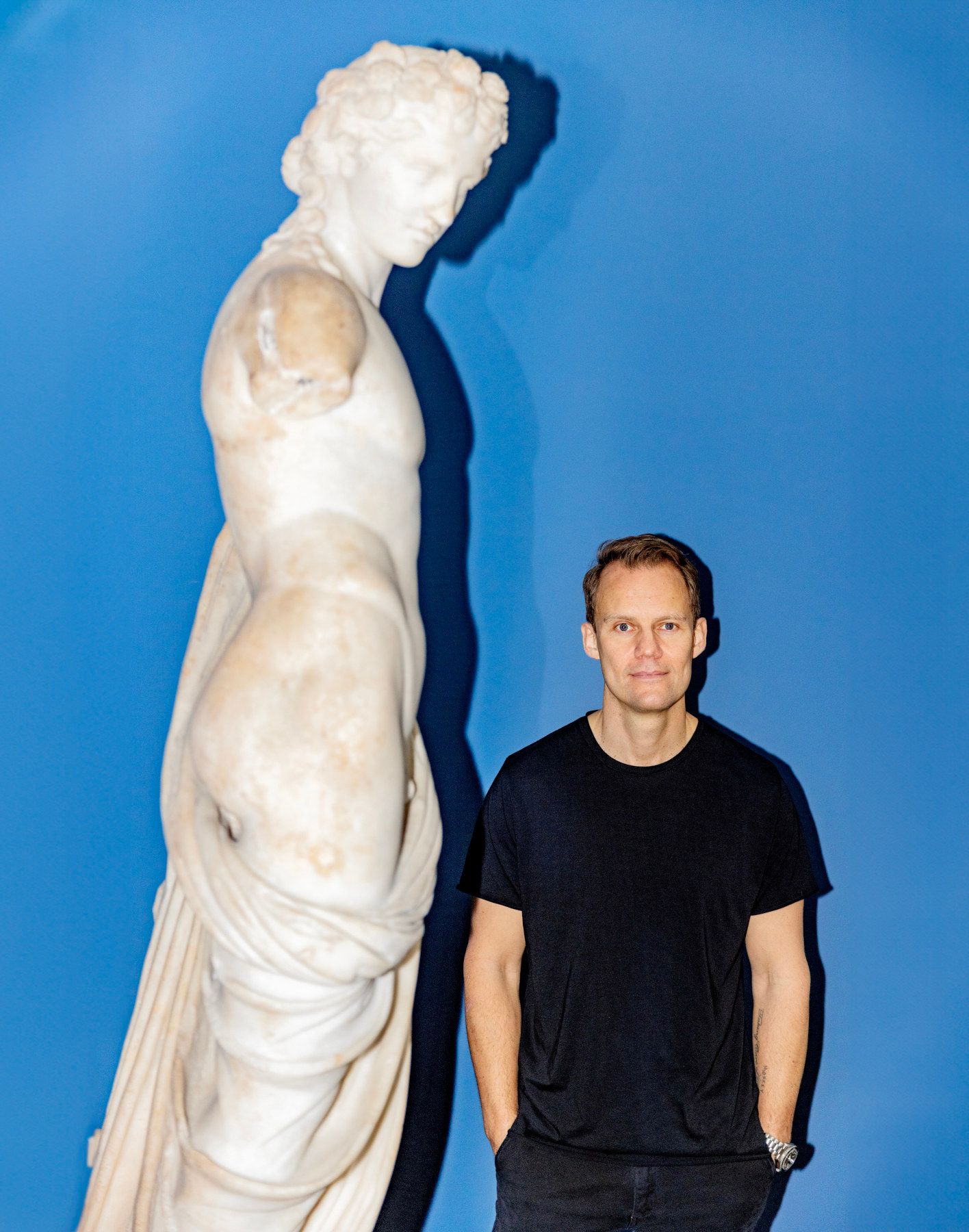 Portrætfoto af Niels Overgaard, mens en muligvis græsk statue tårner sig op ved siden af ham